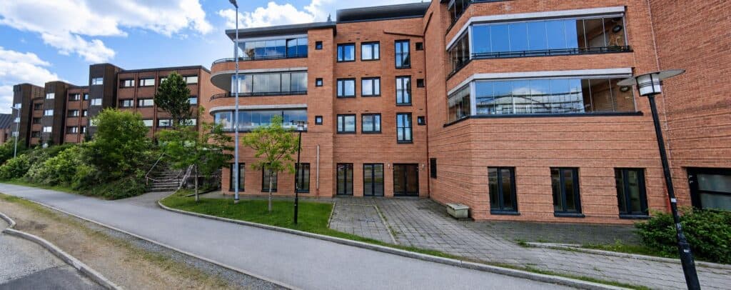 Moderne boligblokk med store balkonger og grøntområder i urbant område.