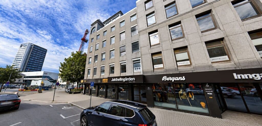 Moderne kontorbygg i sentrum med butikker og parkeringsplass.