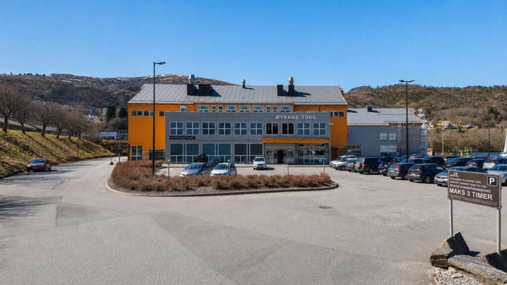 Eksteriør av Eyezone Torg bygning med parkering foran, tydelig blå himmel.