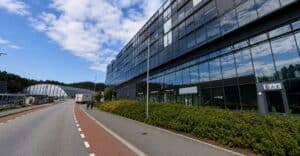 Høyt moderne kontorbygg med glassfasade og grøntområde foran.