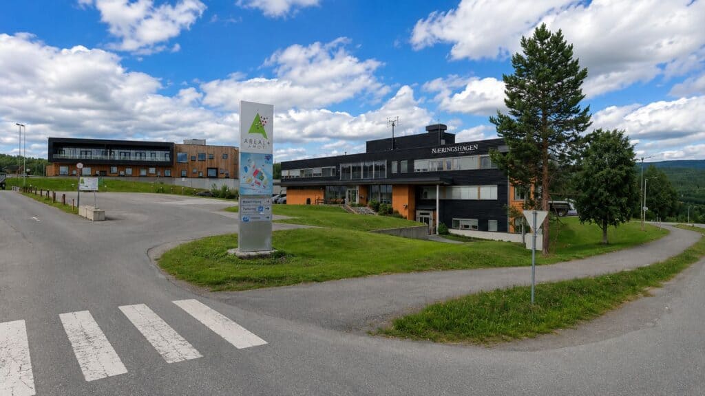 Helsebygg med moderne arkitektur, omgitt av grøntområder og trær, under en klar blå himmel.