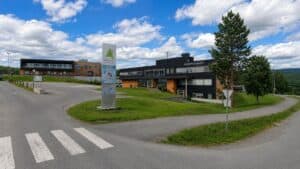 Helsebygg med moderne arkitektur, omgitt av grøntområder og trær, under en klar blå himmel.
