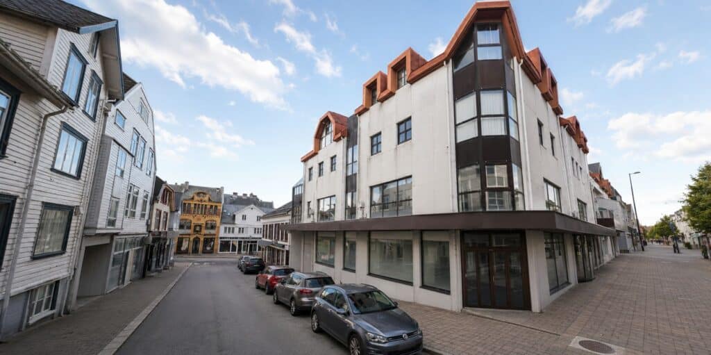 Moderne kontorbygg i sentrum med store vinduer og parkeringsplass.