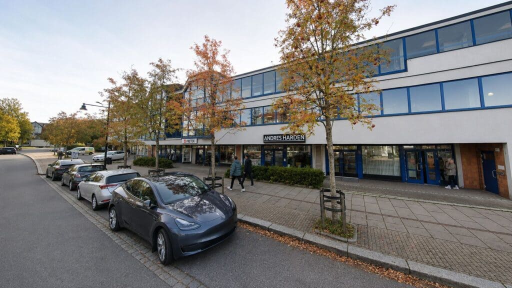Limbra klinikkbygning med parkeringsplasser og høstfargede trær foran.