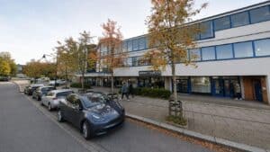 Limbra klinikkbygning med parkeringsplasser og høstfargede trær foran.