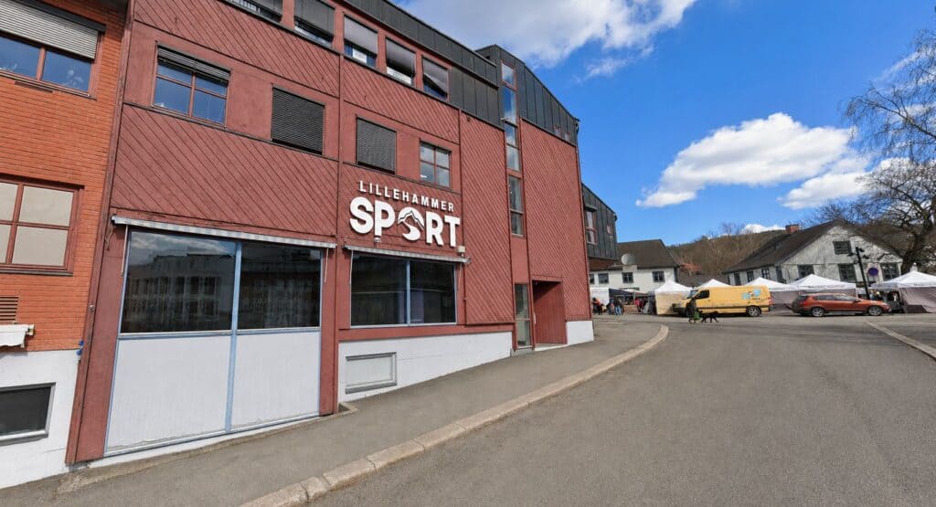 Lillehammer Sport byggning med parkeringsplass og blå himmel.