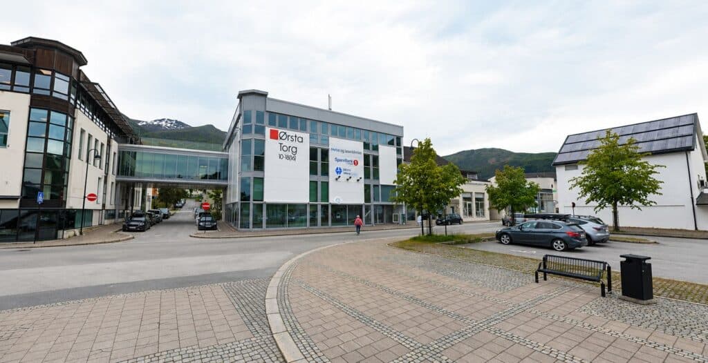 Moderne helsetjenestebygning i sentrum med parkeringsplass og grønne områder.