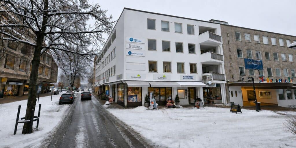 Moderne hvit bygning med butikker i snødekt bymiljø, vintervær.
