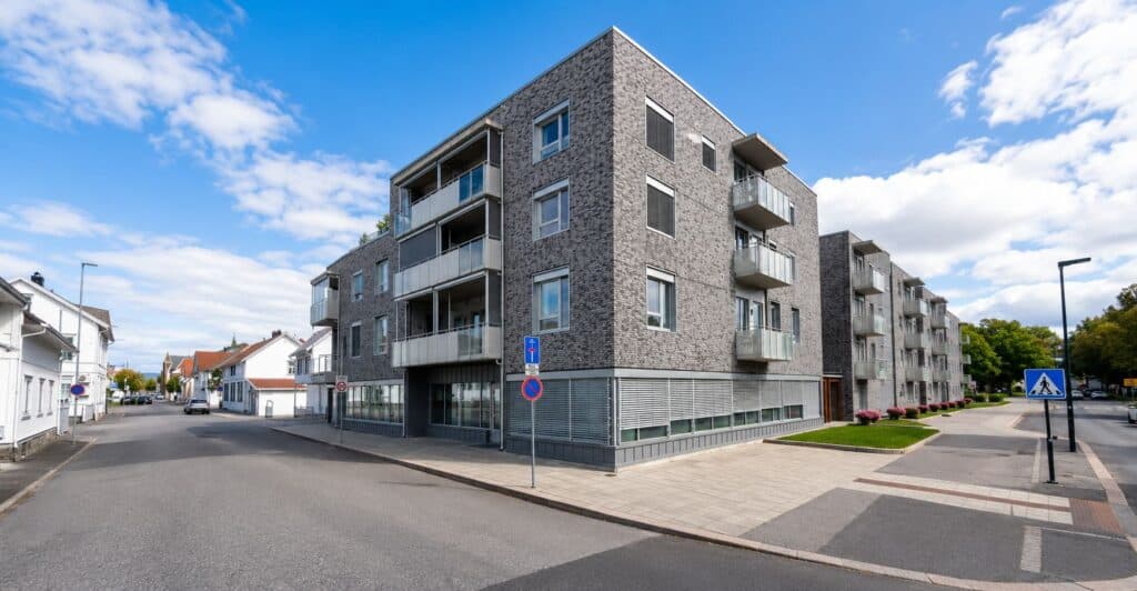 Moderne leilighetsbygg ved veikryss med fortau og parkeringsplass.