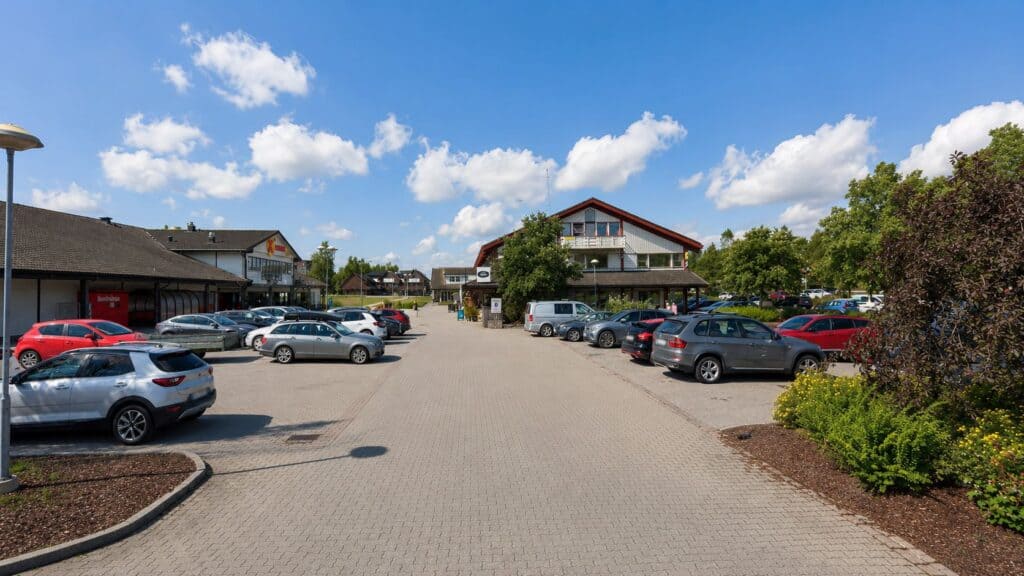 Parkeringsplass foran Limbra klinikk med biler og bygninger under blå himmel.