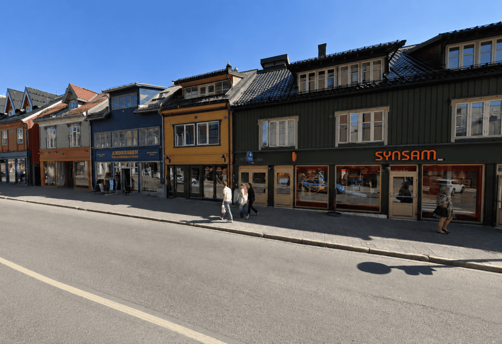 Fargerike trebygninger langs en gate i Tromsø med butikker og mennesker.