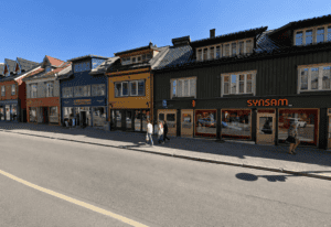 Fargerike trebygninger langs en gate i Tromsø med butikker og mennesker.