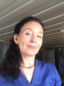 Kvinne i blå arbeidsuniform smiler, innendørs, profesjonell helsepersonell.