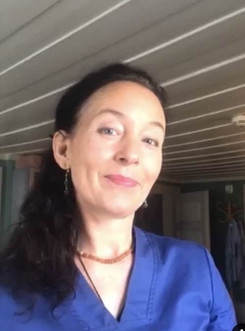 Kvinne i blå arbeidsuniform smiler, innendørs, profesjonell helsepersonell.