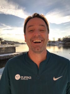 Roy Aune smilende utendørs med vann og himmel i bakgrunnen.