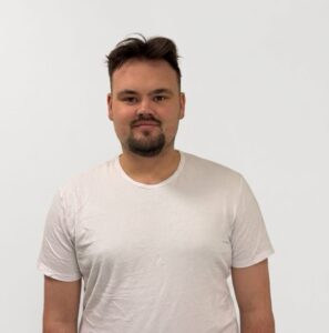 Mann i hvit t-skjorte mot hvit bakgrunn, smilende ansikt.