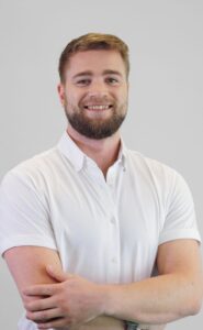 Mann med hvit skjorte smilende med armene krysset, portrett.