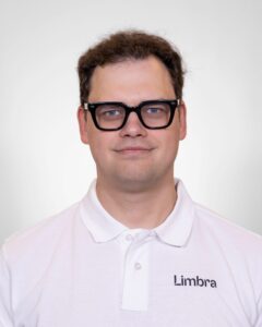 Algirdas Aitman, kiropraktor ved Limbra, smilende med svart briller og hvit polo med Limbra-logo.