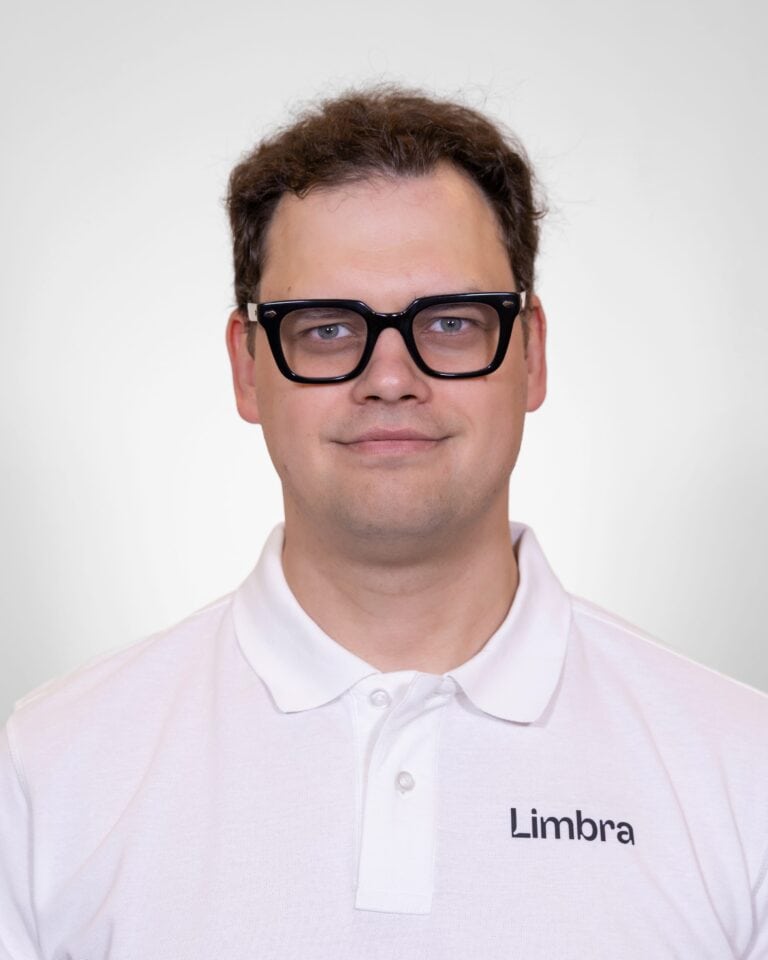 Algirdas Aitman, kiropraktor ved Limbra, smilende med svart briller og hvit polo med Limbra-logo.