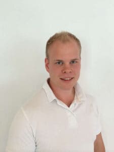 Mann med kort hår og hvit skjorte smiler mot kamera.
