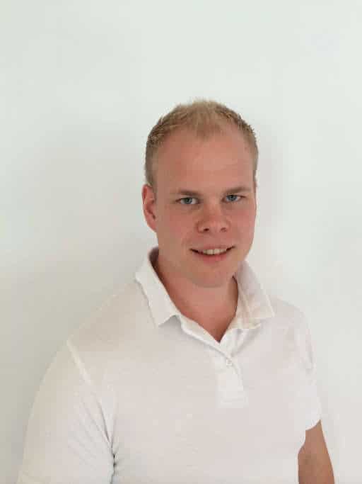 Mann med kort hår og hvit skjorte smiler mot kamera.