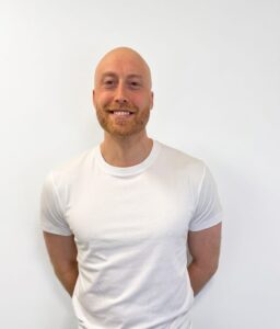 Mann med hvit t-skjorte smilende mot hvit bakgrunn.