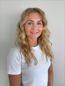 Kvinne med langt, blond hår smilende mot kamera.