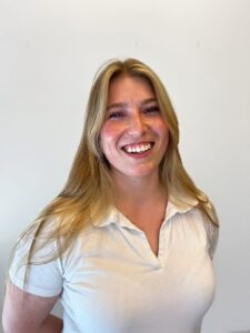 Smilende kvinne med blondt hår i hvit skjorte mot hvit bakgrunn.