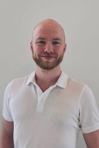 Mann med hvit polo shirt smilende mot kamera, portrett.