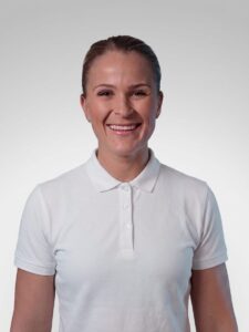 Liten kvinne i hvit polo, smilende, mot lys grå bakgrunn.