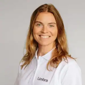 Kvinne med langt, lyst hår smiler mot kamera i hvit skjorte.