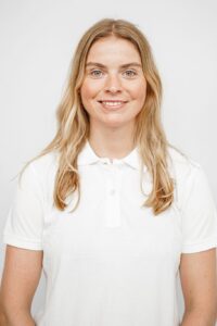 Smilende kvinne i hvit polo, portrett, mot hvit bakgrunn.