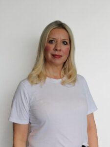 Kvinne med blondt hår i hvit t-skjorte mot hvit vegg.
