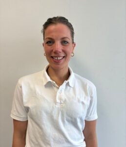 Kvinne smilende terapeut i hvit skjorte foran lys vegg.