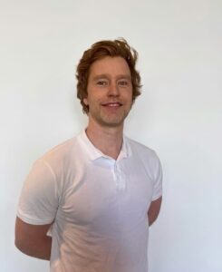 Kvinne smilende mann i hvit polo foran hvit vegg.