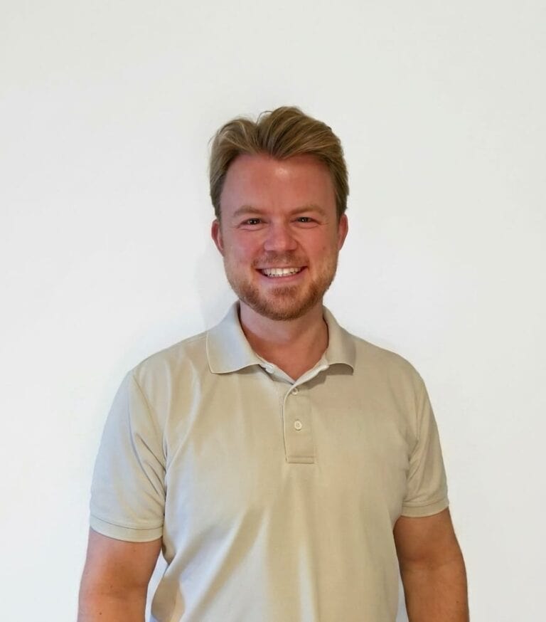 Mann med lyst hår og beige polo shirt smilende mot hvit bakgrunn.
