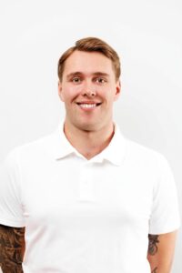Mann med hvit polo smilende mot kamera, portrettbilde.