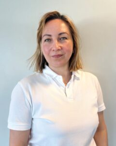 Kvinne i hvit polo shirt foran lys vegg, smilende og avslappet.