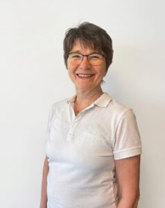 Kvinne smilende kvinne med kort hår og briller, portrett foran hvit bakgrunn.