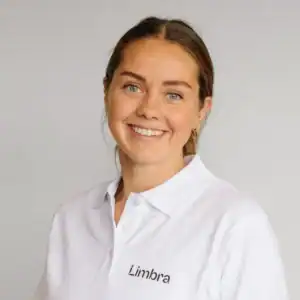 Klinikkansatt smilende kvinne i hvit uniform med Limbra-logo.