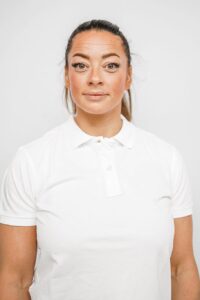 Kvinne med hvit polo-shirt ser direkte inn i kameraet.
