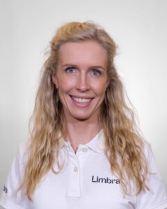 Kvinne med blond hår i hvit Limbraklær smiler mot kameraet.