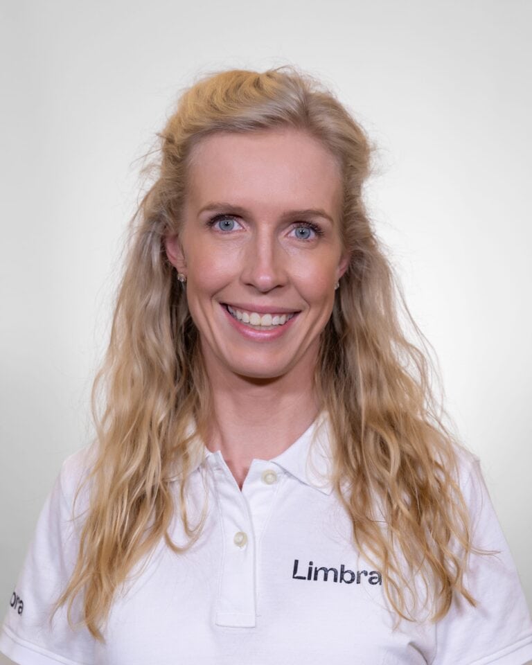 Kvinne med blond hår i hvit Limbraklær smiler mot kameraet.