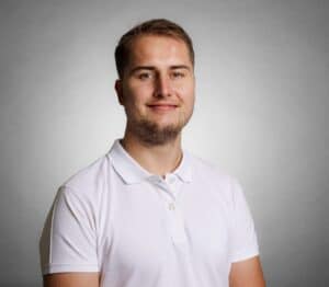 Kvinne i hvit polo-shirt smiler mot kamera, portrettbilde.