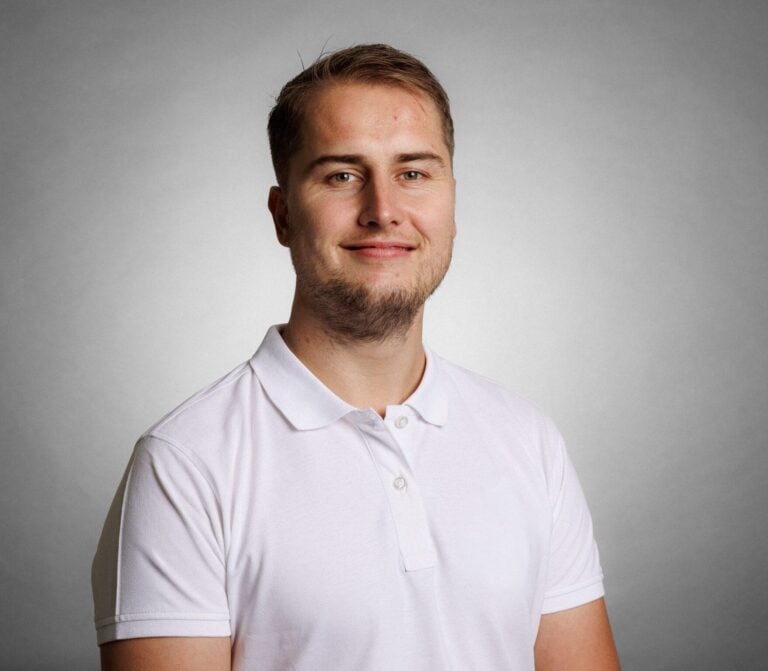 Kvinne i hvit polo-shirt smiler mot kamera, portrettbilde.