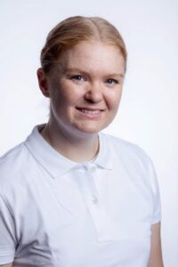 Kvinne med hvit polo smilende mot kamera, portrett.