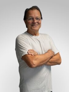 Mann med briller og hvit t-skjorte smilende med armene krysset.