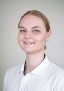 Kvinne med blondt hår og hvit skjorte smilende mot kamera.