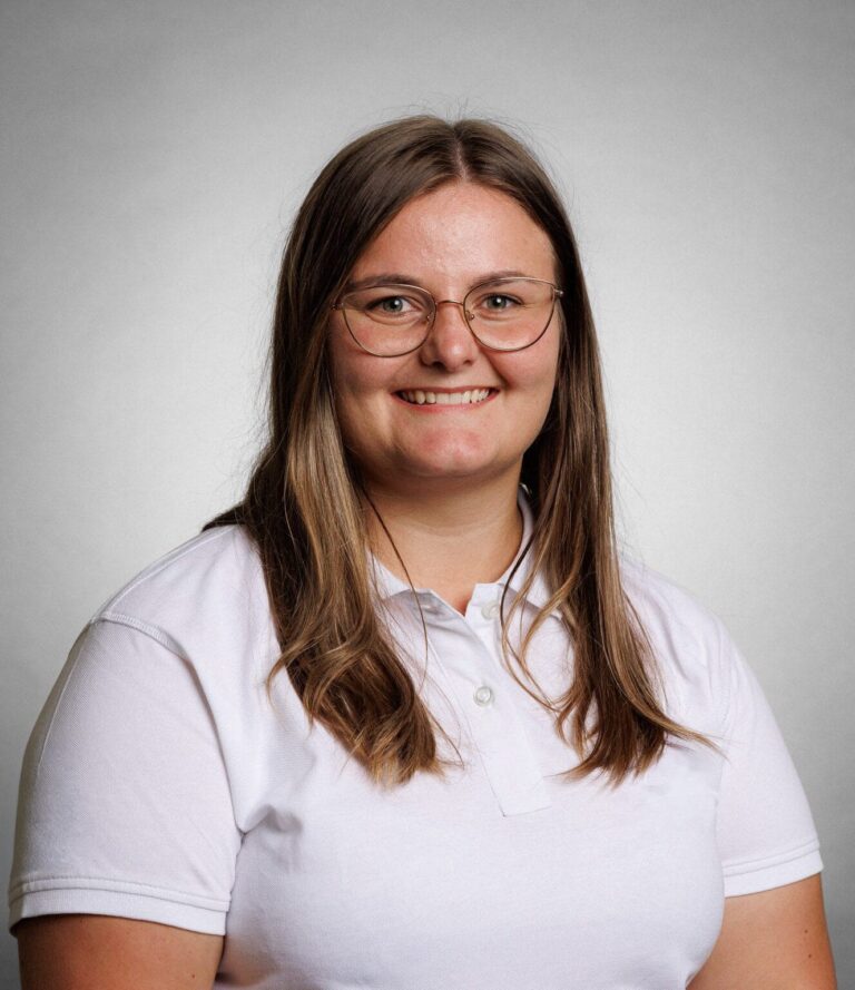 Kvinne med briller smilende i hvit polo, portrett.