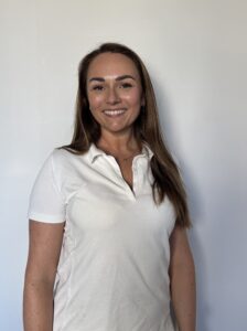 Smilende kvinne i hvit polo, står mot en lys bakgrunn.